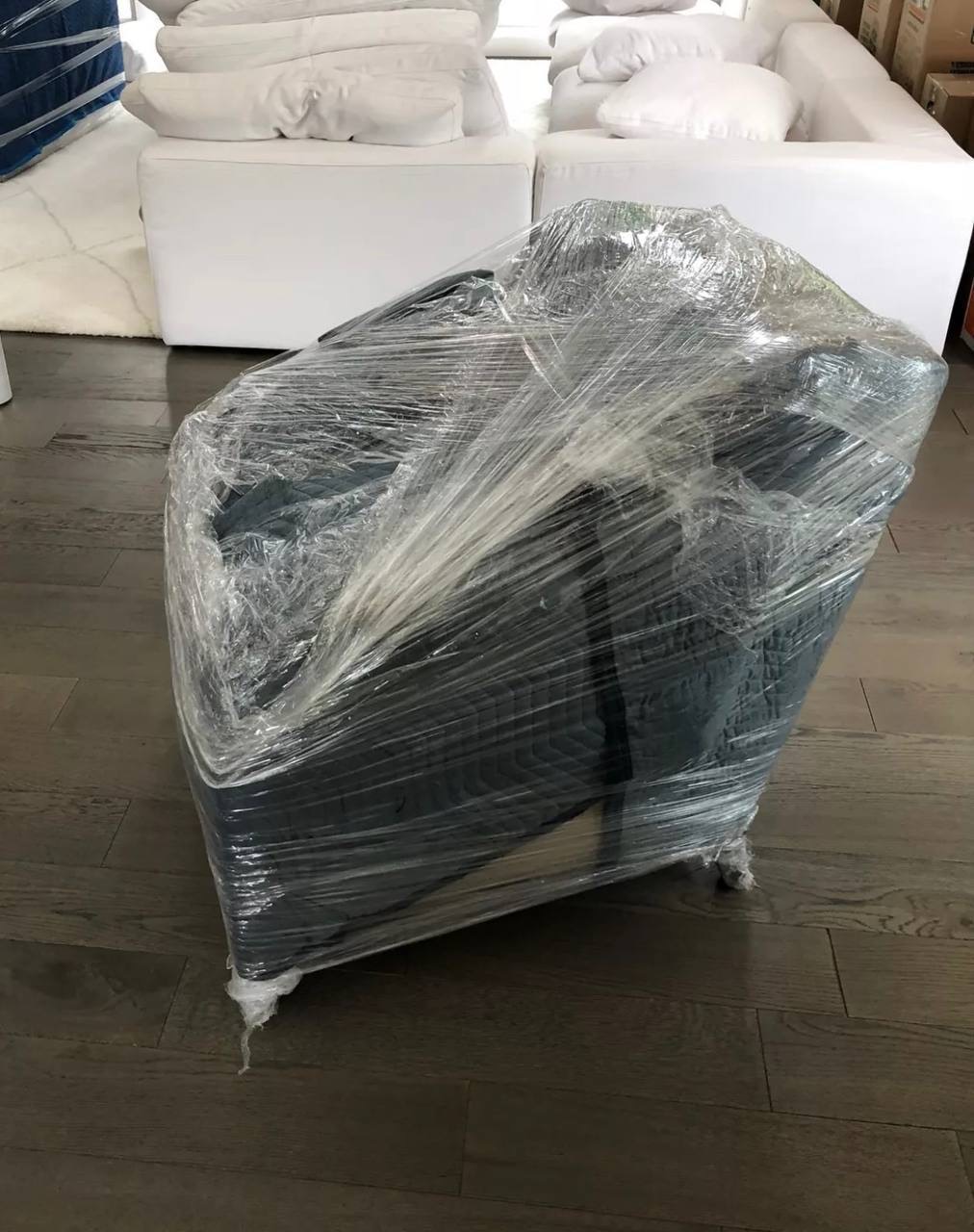 A dark armchair wrapped in protective film inside a bright living room.