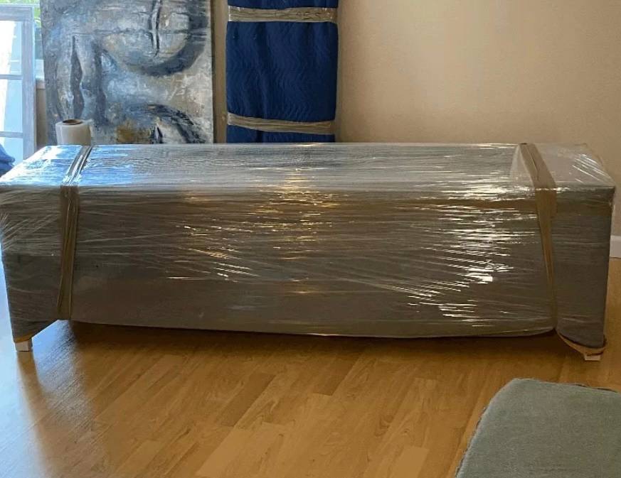 A sofa wrapped in protective film on a hardwood floor before a move.